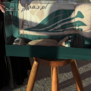 نقصة المحبة الخضراء معروضة في صندوق أكريليك على طاولة خشبية مع سجادة الصلاة الخضراء وبطاقة اسم