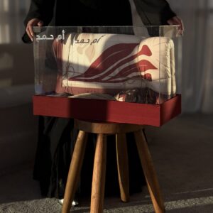 نقصة المحبة العنابية داخل صندوق أكريليك على طاولة خشبية مع سجادة الصلاة العنابية وبطاقة اسم