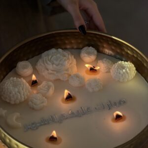شمعة رمضان مضاءة بزهور شمعية منحوتة وكتابة «مبارك عليكم الشهر» في صينية ذهبية