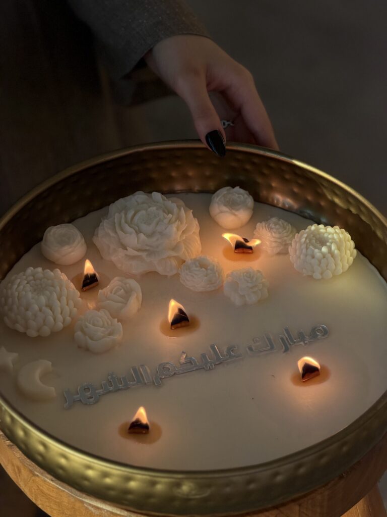 شمعة رمضان مضاءة بزهور شمعية منحوتة وكتابة «مبارك عليكم الشهر» في صينية ذهبية