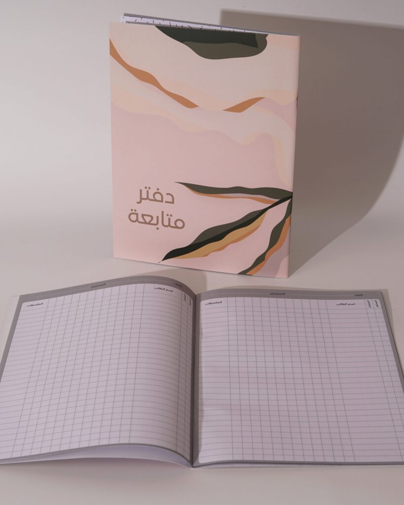 دفتر متابعة ساند بغلاف وردي وتموّجات صحراوية وأوراق نباتية