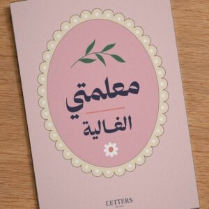 بطاقة إهداء بمقاس A5 عليها رسمة غصن أخضر وزهرة صغيرة على خلفية وردية وعبارة «معلمتي الغالية»، على طاولة خشبية