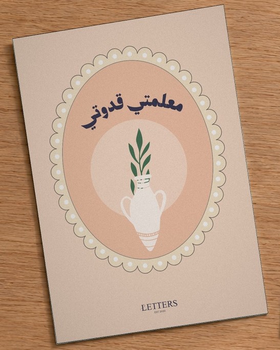 بطاقة إهداء بمقاس A5 عليها رسمة جرّة فخارية بغصن أخضر على خلفية خوخية وعبارة «معلمتي قدوتي»، على طاولة خشبية