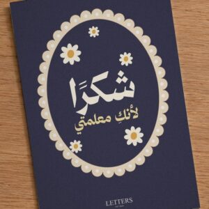 بطاقة إهداء بمقاس A5 عليها رسمة أزهار أقحوان صغيرة على خلفية كحلية وعبارة «شكرًا لأنكِ معلمتي»، على طاولة خشبية