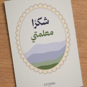 بطاقة إهداء بمقاس A5 عليها رسمة تلال خضراء وبنفسجية وعبارة «شكرًا معلمتي»، على طاولة خشبية
