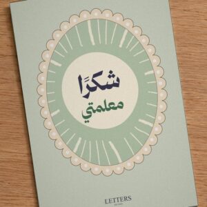 بطاقة إهداء بمقاس A5 عليها رسمة أشعة شمس على خلفية خضراء فاتحة وعبارة «شكرًا معلمتي»، على طاولة خشبية