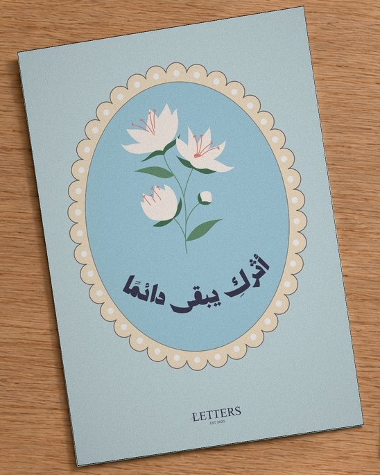 بطاقة إهداء بمقاس A5 عليها رسمة أزهار بيضاء على خلفية زرقاء هادئة وعبارة «أثركِ يبقى دائمًا»، على طاولة خشبية